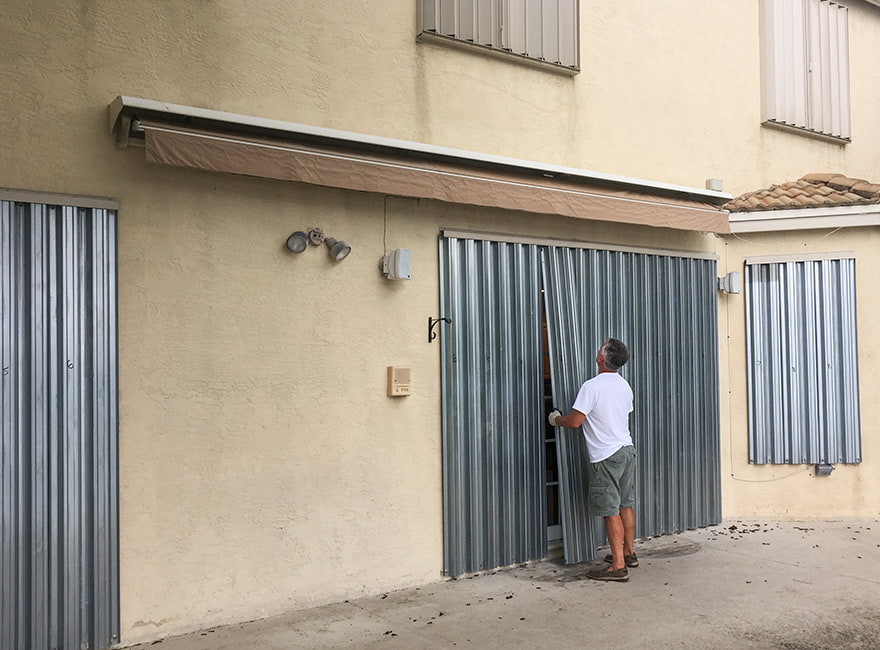 Large metallic hurricane shutters being put up on a home before an upcoming storm.